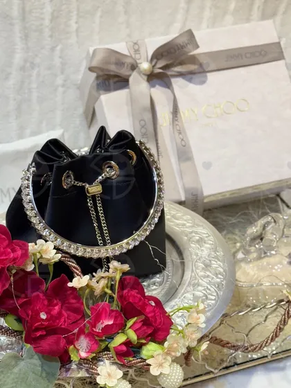 A luxury Jimmy Choo handbag presented on a mirrored tray, adorned with deep red florals. This is how I ensure even the most modern accessories are integrated into the trousseau with elegance and style.