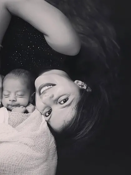 A joyful black and white portrait of a mother and her newborn. The unique angle and genuine smile make this a truly special and heartwarming image.