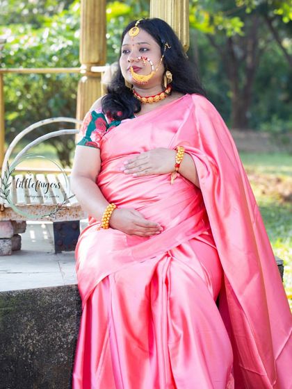 A quiet, contemplative moment during a traditional maternity session. The mom-to-be looks beautiful in her silk saree and ornate nose ring, seated on a bench in the park.