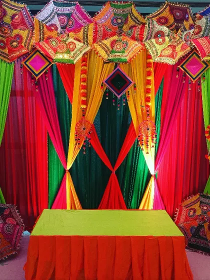 For a traditional godh bharai, I love using vibrant colors. This setup features a backdrop of bright drapes in green, pink, and yellow, topped with beautiful Rajasthani embroidered umbrellas for a truly festive look.