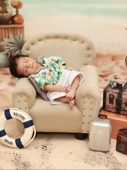 This 'Tiny Traveler' is on vacation. A newborn relaxes on a miniature sofa on a sandy beach set, complete with a tiny suitcase, radio, and other travel-themed props for a creative and fun shot.