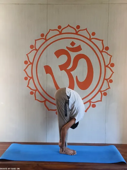 A student practices Padahastasana (Hand to Foot Pose), a forward bend that calms the mind and stretches the entire back side of the body.