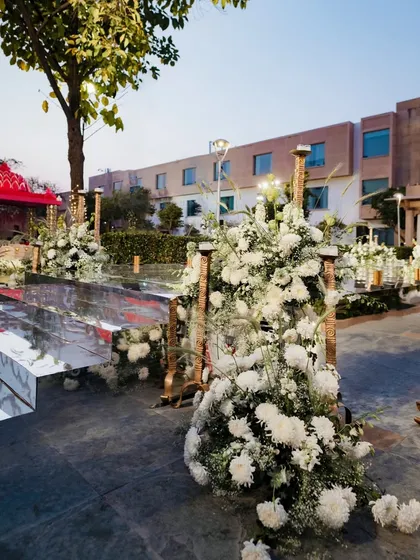 A side angle of the mirrored walkway, showing how it reflects the sky and the surrounding white floral decor. This design element adds a modern, glamorous touch to the traditional Varmaala ceremony.