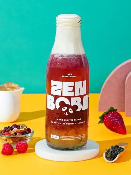 A single bottle of Zen Boba's strawberry flavor, styled with fresh ingredients against a colorful, split-tone background. This shot clearly communicates the natural elements of the product for packaging or ads.