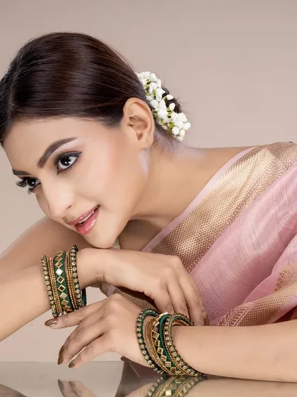 This image features a model wearing traditional green and gold bangles, paired with a pink silk saree and jasmine flowers in her hair. The composition evokes a sense of timeless grace, ideal for festive jewellery campaigns.