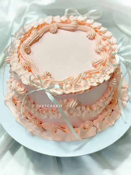 An elegant vintage-style cake with delicate, Russian-style piping techniques. The peach color and ribbon details give it a soft, romantic feel.