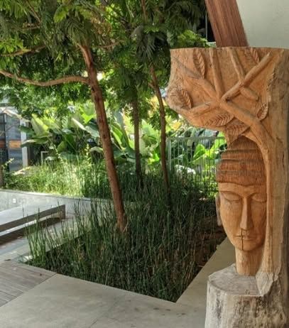 A serene, carved wooden sculpture stands as a focal point at the edge of a planter box filled with tall grasses. Integrating art into the landscape adds a layer of personality and soul.