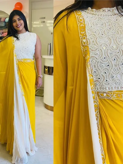 A stunning combination of yellow and white, this draped gown features a heavily embroidered boat-neck blouse. It's a fresh and elegant Indo-Western look perfect for a summer wedding or party.