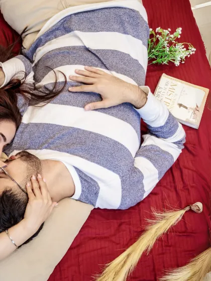 A tender moment captured from above. The couple shares a kiss while lying on a bed, creating a romantic and artistic pre-wedding photograph.