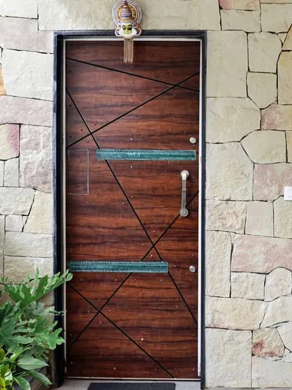 The main entrance door features a modern geometric pattern with resin inlays, set against a rugged random rubble stone wall. This contrast of textures makes for a memorable entry.