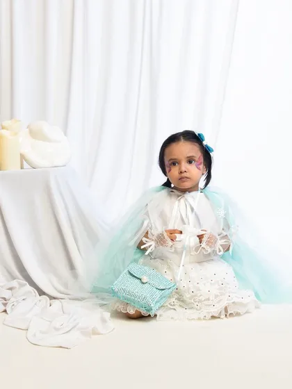 A child model seated in a white and green fairy costume, holding a small purse.
