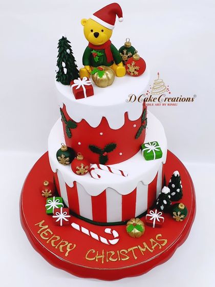 A whimsical two-tier Christmas cake with a festive teddy bear, edible ornaments, and candy cane stripes.