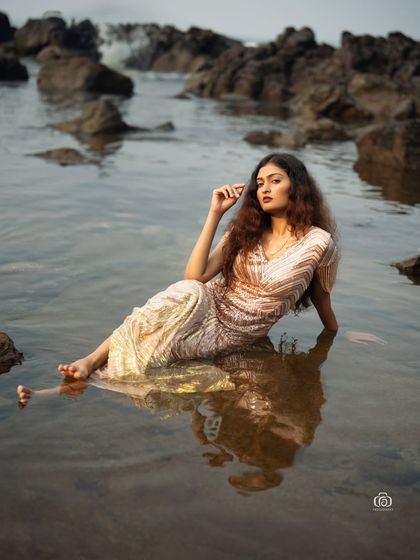 A serene moment captured in the shallow waters of the beach. The model's reflection in the water and the soft light on the sequined dress create a magical, ethereal feel.