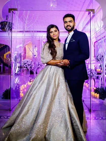 A classic reception portrait of a couple, with the bride in a shimmering silver gown and the groom in a sharp navy suit.