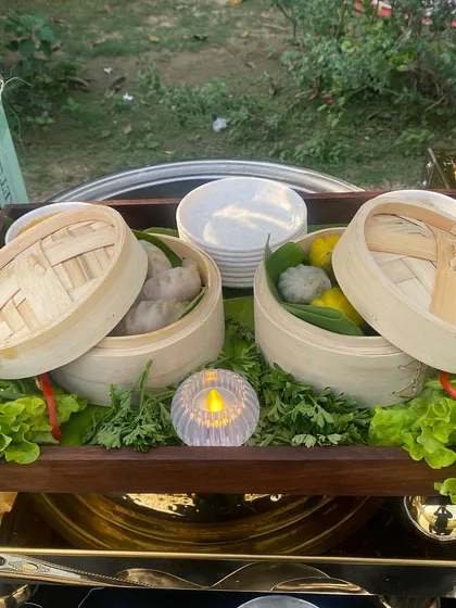 A close-up of our steamed dim sum, presented in traditional bamboo steamers. We serve a variety of fillings, ensuring there is a delicious option for every guest, garnished with fresh greens and lit by a candle for ambiance.