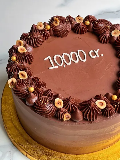 A close-up of a rich chocolate hazelnut cake, decorated with piped swirls and toasted hazelnuts. This one was for a huge corporate milestone.