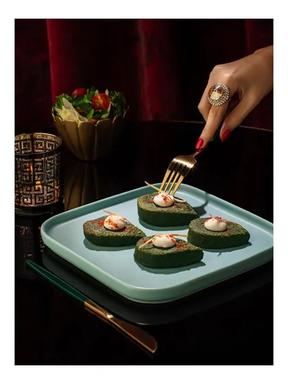A sophisticated shot for Club Jolies, featuring elegantly styled avocado appetizers. The use of a hand with fine jewelry and red nails adds a touch of glamour and luxury to the dining experience.