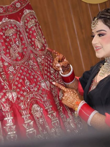 The bride admiring her beautiful red lehenga. This is a classic getting-ready shot that captures the bride's excitement and love for her wedding day attire.