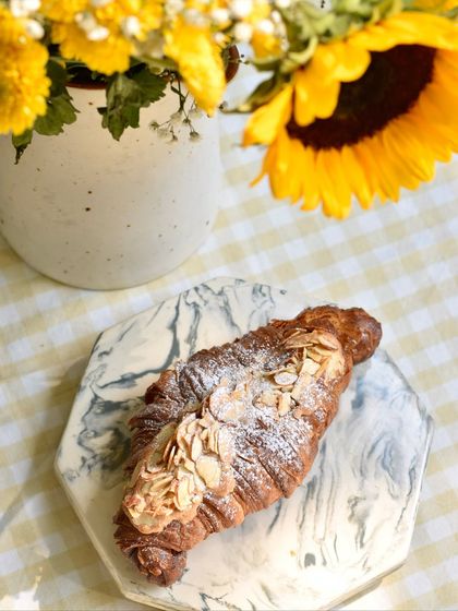 A freshly baked Twice-baked Almond Croissant, dusted with powdered sugar. This classic pastry is filled and topped with a rich almond cream and sliced almonds for extra flavour and crunch.