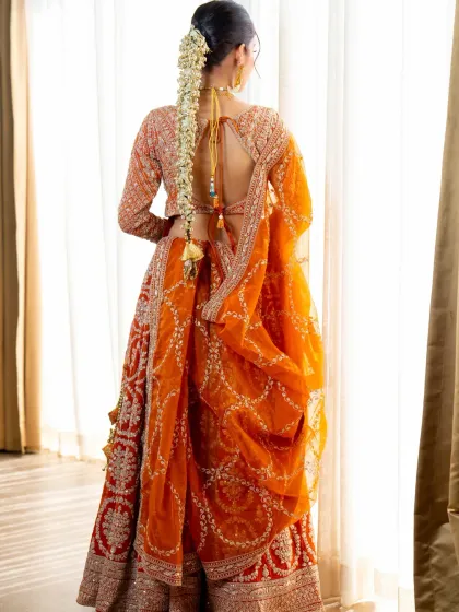 The back of a lehenga is just as important as the front. This view shows the beautiful back design and the flow of the orange dupatta on our traditional bridal lehenga.