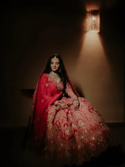 A full-length portrait showcasing the magnificent bridal lehenga. The single light source creates a dramatic, spotlight effect, making the bride the absolute center of attention.