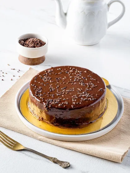 A decadent double chocolate cake with a glossy ganache finish. The bright, clean lighting on a white marble surface gives it a modern and luxurious feel, perfect for a high-end patisserie.
