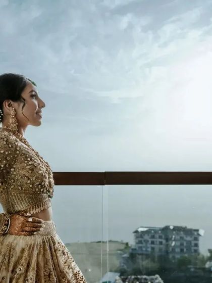 A sun kissed portrait of the bride on a balcony. The natural light highlights her features and the intricate details of her golden outfit, creating a warm and glowing image.