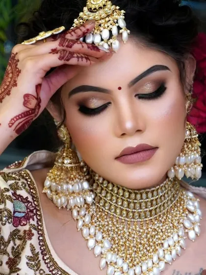 A close up of a bride wearing a stunning gold-plated kundan choker set, heavily embellished with pearls. This Punjabi-inspired bridal set includes a matching maang tikka and oversized jhumkas for a complete and elegant look.
