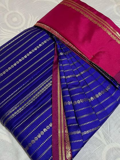 A beautiful royal blue saree with silver stripes and a bright pink border. The pleats are set to show off the lovely color combination.