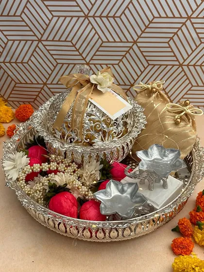 This silver tray hamper is a classic choice for Diwali. It’s artfully arranged with a decorative silver bowl, traditional elephant-shaped diyas, and small potlis, all surrounded by fresh marigold flowers.