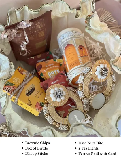 A closer look at the contents of our festive potli hamper. It includes delicious brownie chips, a box of brittle, dhoop sticks, and two beautiful tea lights, all arranged in a delicate, ruffled potli.