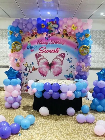 A butterfly and unicorn theme for a birthday party. This setup includes a custom backdrop, a cake table surrounded by balloons, and balloon pillars.