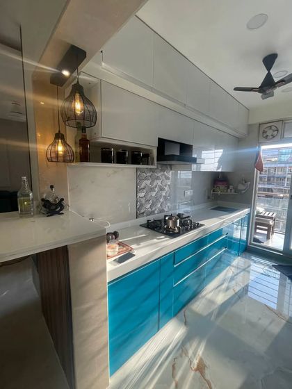 An angled shot capturing the morning light hitting the glossy blue cabinets, showcasing the breakfast counter and the seamless flow of this open-plan kitchen.
