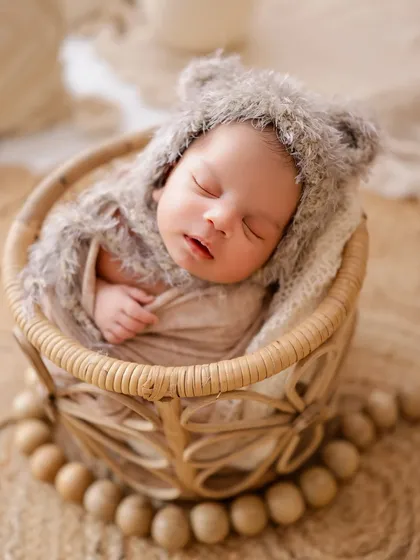 I love capturing newborns in their sleepy, peaceful state. This little one is nestled in a soft basket, wearing an adorable fuzzy bear hat from my studio's collection.