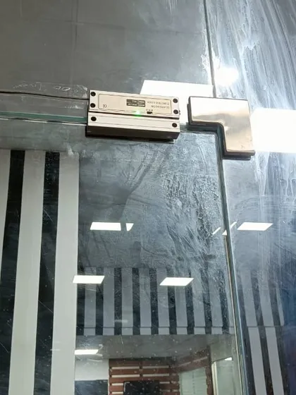 This is an electromagnetic (EM) lock with an L-bracket, installed on a glass door. This type of lock is powerful and reliable for securing frameless glass entrances in offices and commercial buildings.