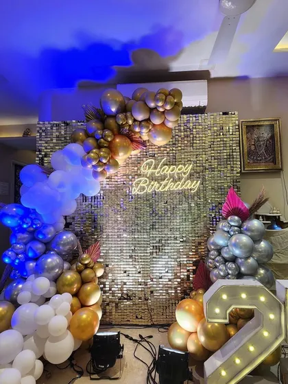 Another angle of the 25th birthday shimmer wall setup. The blue uplighting adds a cool contrast to the warm gold tones of the balloons and backdrop, showing how lighting can change the mood.