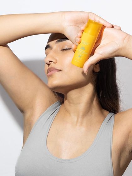 A serene and aspirational lifestyle shot. The model's relaxed pose and the way she holds the product to her skin convey a sense of calm and self-care.
