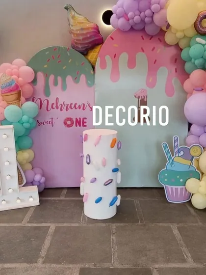 A "Sweet One" first birthday party with an ice cream theme. The decor includes colorful backdrops shaped like melting ice cream, fun cutouts, and a light-up number '1'.