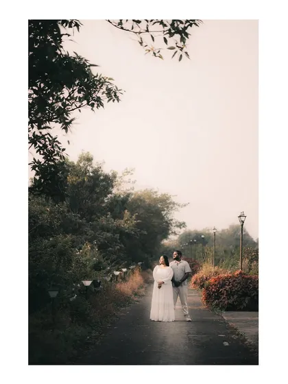 A wide shot of a couple standing on a misty path in Tamhini Ghat, capturing the scale and beauty of the natural surroundings.