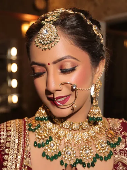 A classic bridal pose showing the harmony between the makeup and the entire look. The defined eyes, red bindi, and matching lip color tie together perfectly with the traditional red and gold bridal attire.