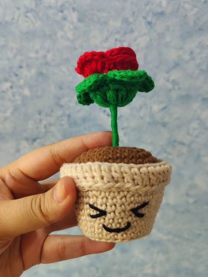 This tiny rose pot is the perfect little accessory for your desk or a small shelf. The rose is a vibrant red, and the pot has a cute winking face, adding a touch of fun.