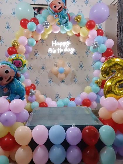 A Cocomelon-themed second birthday setup for a home celebration, using a colorful balloon ring and character foil balloons.