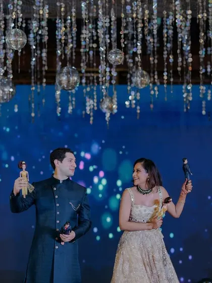 A fun moment on stage during the Sangeet, with the couple holding up Barbie and Ken dolls, adding a playful and personal touch to their celebration.