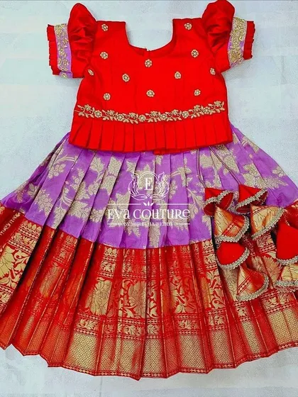 A newborn-sized Pattu Pavadai in red and purple. The blouse has a pleated peplum, and the skirt has a rich gold border.