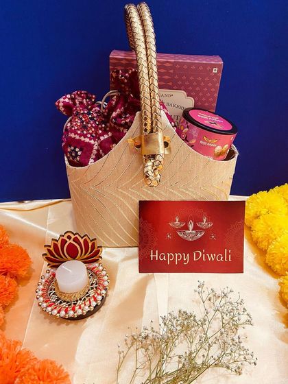 A beautiful beige basket with ornate golden handles, filled with sweets and a decorative lotus candle. This hamper is a blend of traditional and contemporary design.