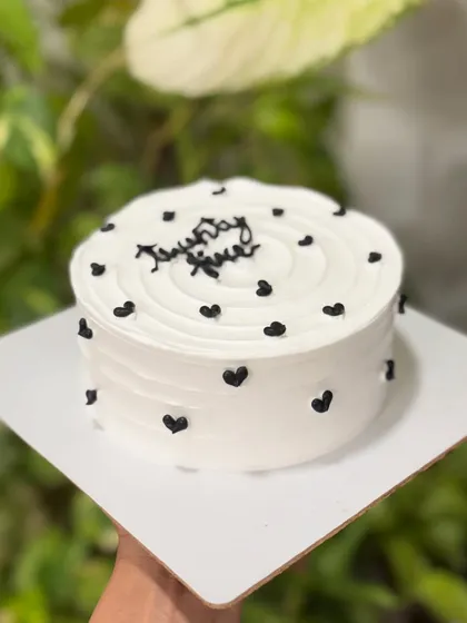 Minimal, chic, and effortlessly aesthetic. This monochrome cake features a clean white buttercream base with a swirl top and is dotted with tiny, elegant black hearts.