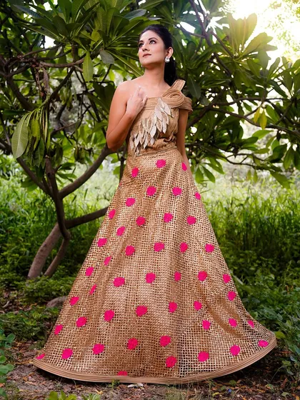 A beautiful outdoor shot of a model in a unique jute-like gown with pink polka dots. The natural setting provides a lovely contrast to the unconventional material of the dress.