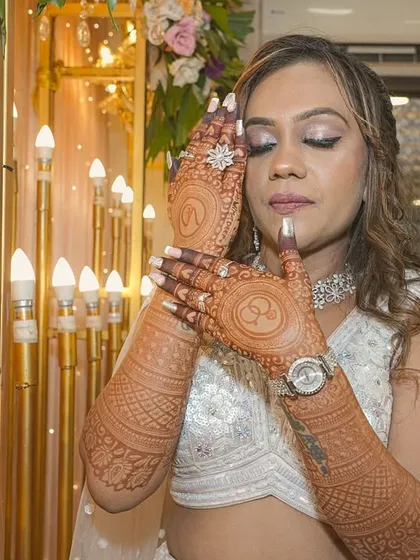 A portrait of a happy client at her engagement, showcasing her full-sleeve mehendi. The rich color and detailed patterns on her arms and hands complement her festive attire perfectly.