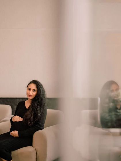 A solo portrait from the same indoor session. The artistic framing, shooting through a foreground element, adds depth and a sense of quiet intimacy to the photograph.
