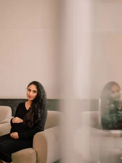 A solo portrait from the same indoor session. The artistic framing, shooting through a foreground element, adds depth and a sense of quiet intimacy to the photograph.